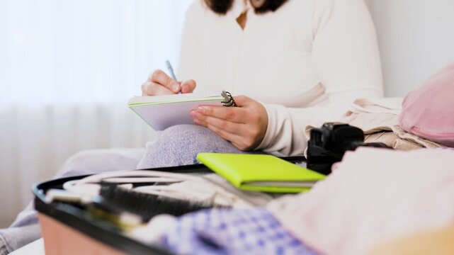 Woman doing travel preparation for a summer vacation. She writes a packing list and puts her passport into her suitcase, enjoying the exciting vacation mood. High quality 4k footage