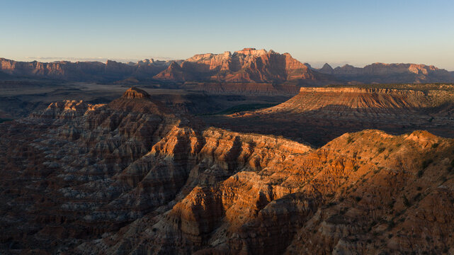 Aerial view of Zion National Park featuring rugged red rock canyons, layered mesas, and desert landscape under warm golden hour light, Washington County, Utah, United States.