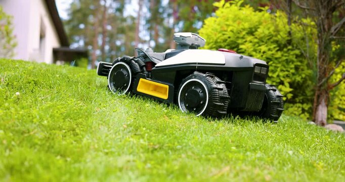 Robotic lawn mower working at garden cutting lush green grass on a slope. Automated lawn care