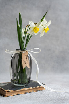 Close-up of a bunch of daffodils in a vase with a thank you gift tag on an old book