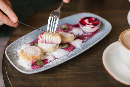 Close-up of a man sitting at a table eating cottage cheese pancakes (syrniki) with cream and blueberry jam
