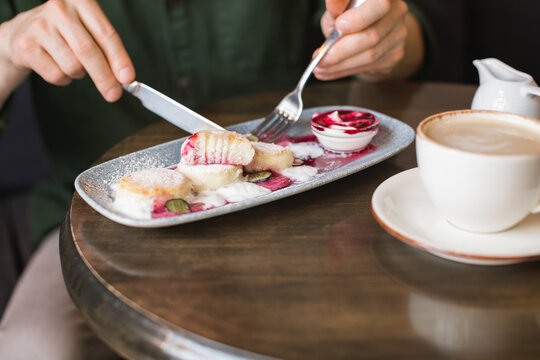 Close-up of a man sitting at a table eating cottage cheese pancakes (syrniki) with cream and blueberry jam