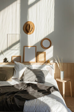 Cosy sunlit bedroom with natural shadows on a collection of assorted blank picture frames hanging over a double bed