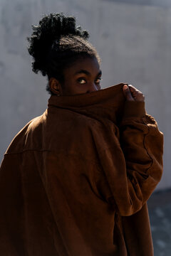 Portrait of a mysterious Black woman standing outdoors on a sunny day hiding her face behind her jacket collar