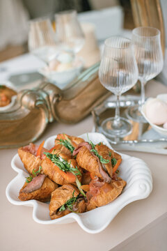 Savory croissants with roast beef, arugula, and tomatoes on a white shell-shaped plate.