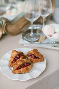 Close-up of sweet croissants with cherry filling on a table with wine glasses and meringues