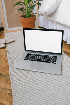 Open laptop with a blank screen on a rug next to a double bed in a bedroom