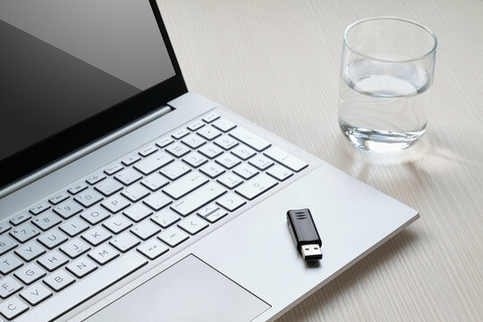 Laptop keyboard with glass of water on wooden desk, modern workspace setup for technology, data storage, office and business concepts