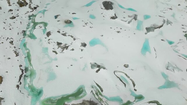 Aerial drone shot revealing the icy landscape of Austerdalsbreen Glacier in Norway with turquoise glacier pools, emerald meltwater, moraine, and glacier tongue.