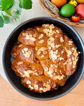 Overhead view of a loaf of Freshly baked traditional Bulgarian Easter bread (Kozunak) with flaked almonds on a table next to a bowl of colourful Easter eggs
