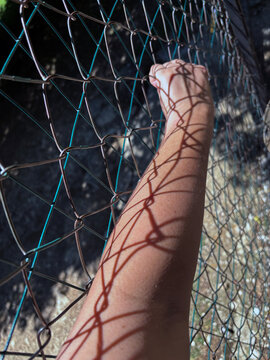 Close-up of a person's hand standing outdoors holding onto a metal fence