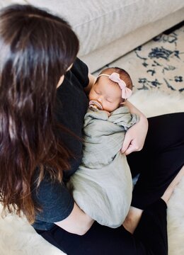Overhead view of a woman sitting cross-legged on the floor holding her newborn baby daughter