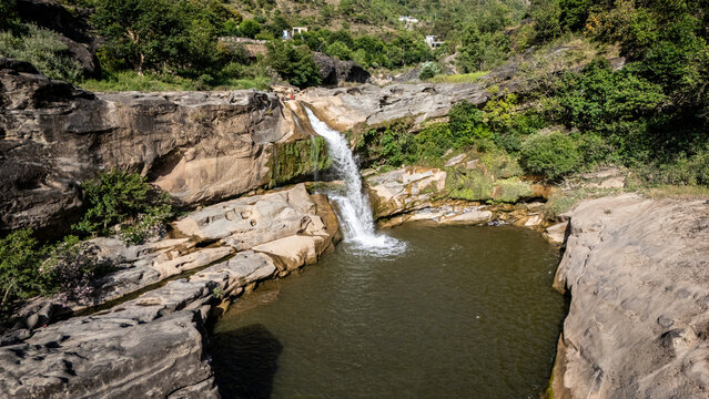 Aerial view of Mahuli Gulpur Waterfall cascading over rugged rocky cliffs into a natural pool surrounded by lush green hills and dense vegetation Kotli, Azad Kashmir, Pakistan.