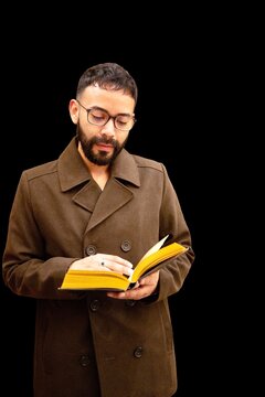 Portrait of a Mid adult man wearing a peacoat standing in front of a black background reading a hardback book