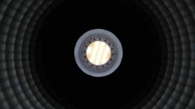 A close-up view directly inside a studio lighting reflector focusing on the central bright LED chip. The textured silver interior creates concentric circular patterns of light and dark