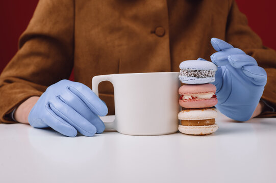 Close-up of a woman wearing gloves sitting at a table with a cup of coffee and stack of assorted macarons