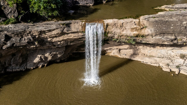 Aerial view of Mahuli Gulpur Waterfall cascading over a rocky ledge into a natural pool surrounded by green vegetation in Kotli, Azad Kashmir, Pakistan.