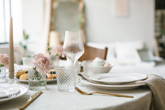 Elegant table setting with gold cutlery, ribbed glassware, linen textiles and pink carnations in a dining room