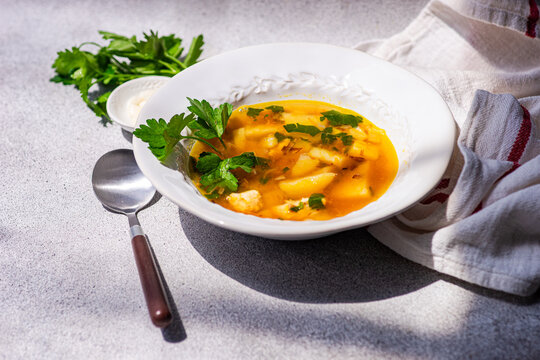 Close-up of a bowl of Healthy chicken soup with potatoes, carrots, parsley and fresh garlic cloves on a table with a  tea towel