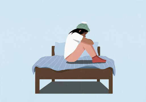 Sick woman sitting on bed with an ice pack on her head