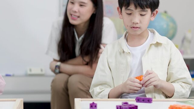 Asian Boy Student Playing with Plastic Blocks in Classroom with Teacher