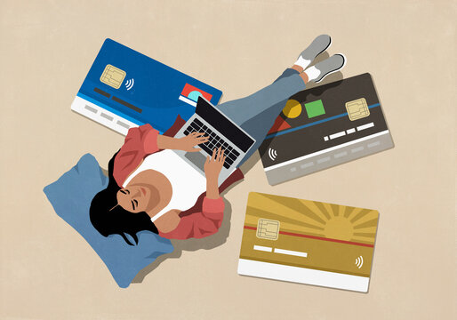 View from above woman online shopping at laptop surrounded by large credit cards