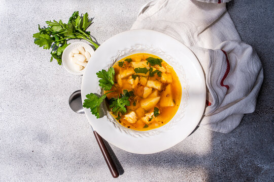Close-up overhead view of a bowl of Healthy chicken soup with potatoes, carrots, parsley and fresh garlic cloves on a table with a wine glass and tea towel