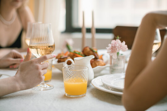 Close-up of three women sitting at a dining table drinking white wine, orange juice and eating savoury croissants