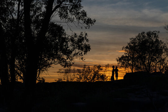 Silhouetted mother and son below trees against sunset sky, Darwin, Australia