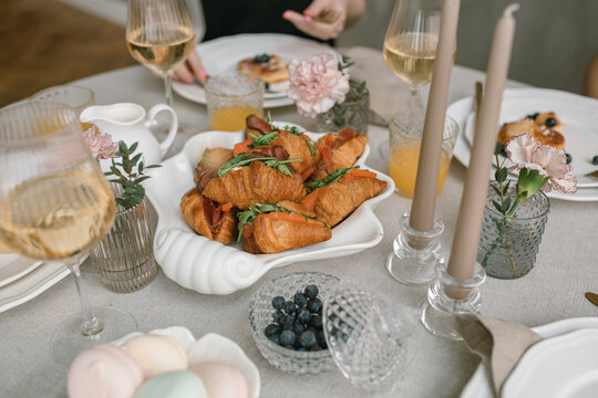 Close-up of fresh croissant sandwiches with roast beef, rocket and tomatoes, blueberries, meringues and glasses of white wine on a dining table