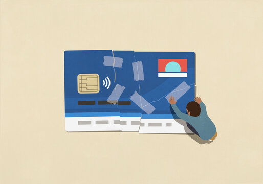 View from above of man attempting to fix broken credit card with adhesive tape