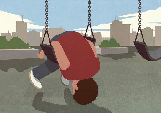 Boy folded over swing on playground in urban park