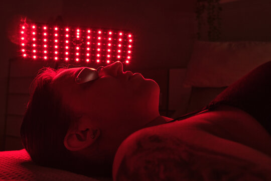 Young woman receiving red light therapy treatment from an led panel, promoting skincare and anti-aging