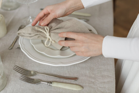 Close-up side view of a woman standing at a dining table setting the table for a dinner party
