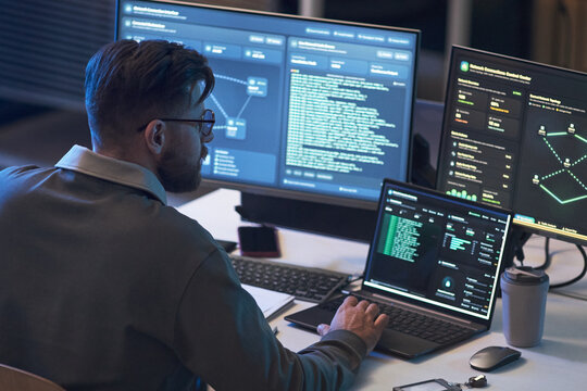 Young adult Caucasian man monitoring code and network dashboards across multiple screens, analyzing cybersecurity data. Ideal for IT security, software development, data protection marketing