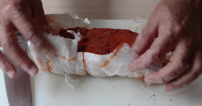 Male hands removing wrapping from homemade pork cured meat covered with spices and paprika, then cutting it in half and showing the inside to camera. Close up food preparation scene.