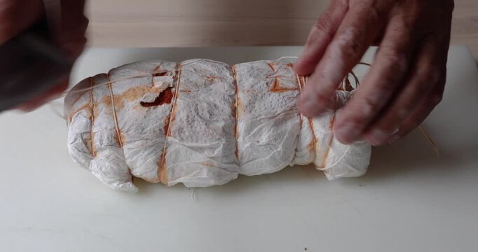 Cutting String Around Homemade Pork Cured Meat with Knife on White Cutting Board, Close Up. Male hands cutting the string around homemade pork cured meat with knife on white cutting board. 