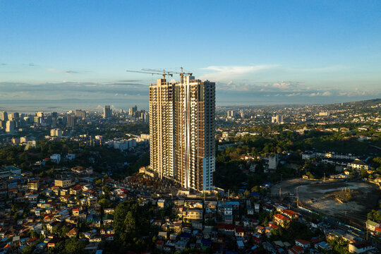 Aerial view of a modern skyscraper under construction with cranes on top overlooking the dense urban landscape and residential rooftops Cebu City, Central Visayas, Philippines.