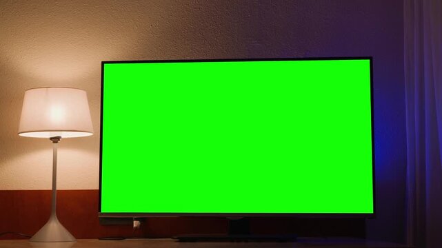 Hotel room interior with television displaying green screen mockup. Modern hospitality scene ideal for chroma key replacement, digital advertising, screen mockup and travel accommodation concepts