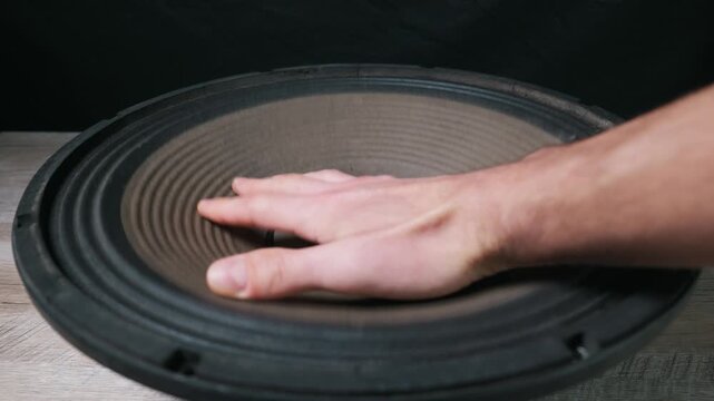Male hand presses on the flexible cone of a large professional audio subwoofer speaker. Concept of bass frequency, haptic feedback, audio engineering, and testing sound equipment.