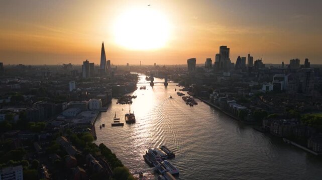 Establishing aerial view of the skyline of London, United Kingdom, along the Thames river with City and Tower bridge during a golden summer sunset