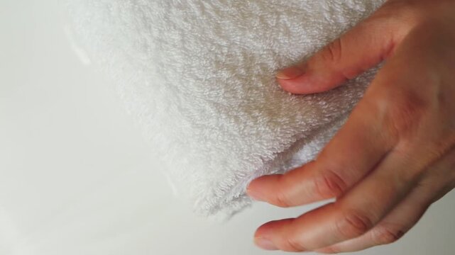 A close-up of a hand placing a fresh white towel on a stack of neatly folded towels, gently smoothing the soft fabric. Concept of hotel service, cleanliness, hospitality, and fresh linens. High