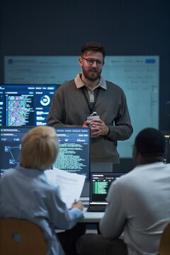 Vertical shot of Caucasian young adult man leading software team meeting, presenting coding workflow to colleagues in office. Ideal for cybersecurity, IT training, agile development