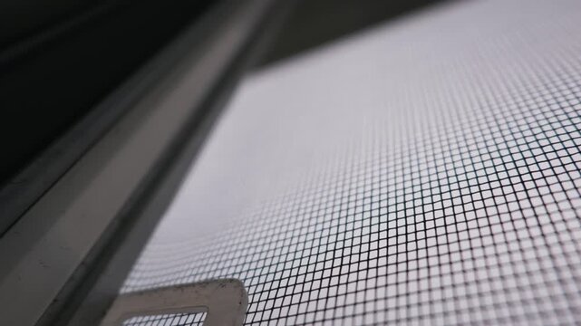Macro view of a white mosquito net mesh against a dark window frame. This concept focuses on summer insect protection, ensuring pests remain outdoors and providing a barrier against
