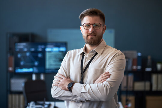 Portrait of Caucasian young adult businessman standing with crossed arms in office, looking at camera and conveying confidence. Ideal for leadership, corporate profile, recruitment marketing