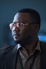 Fototapeta premium Vertical shot of Black middle aged businessman wearing eyeglasses, looking away with focused expression during corporate event. Suitable for leadership, strategy, executive branding