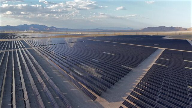 Aerial view of a massive solar panel array stretching across the desert landscape under a cloudy sky near Enterprise, Nevada, United States.