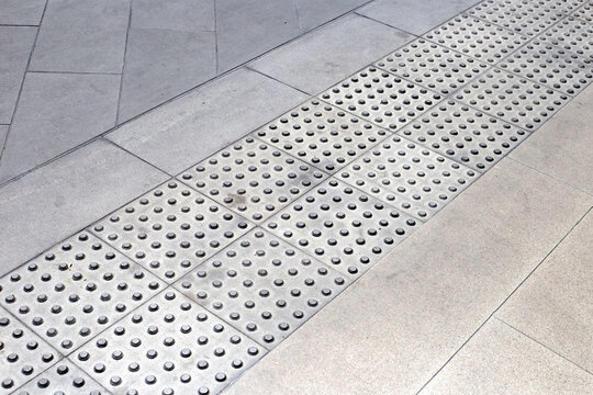 Tactile paving path with warning bumps for visually impaired people on a city sidewalk.