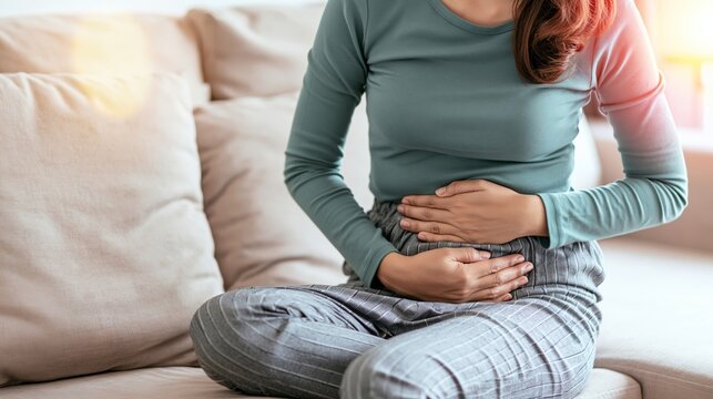 Woman suffering from stomach ache, sitting on a sofa, highlighting menstrual cramps, digestion problems, or related health issues