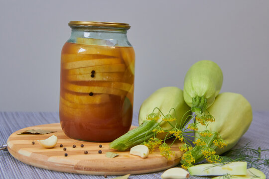 Pickled zucchini in a glass jar and fresh vegetables, Concept of homemade canning, winter food preservation, and traditional rustic recipes.